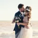 A bride and groom kissing at the beach.