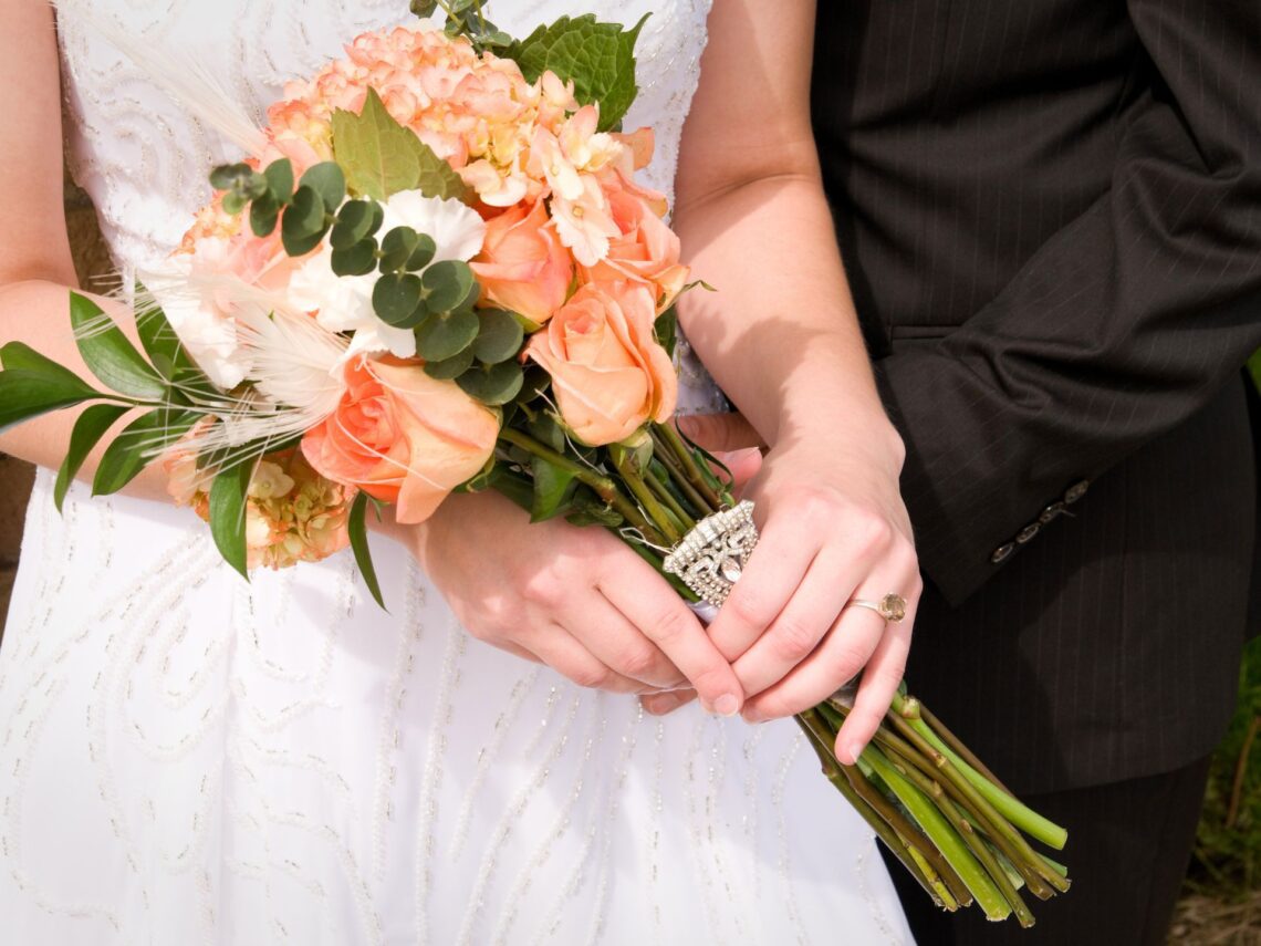 A bride carrying a peach colored wedding bouquet.