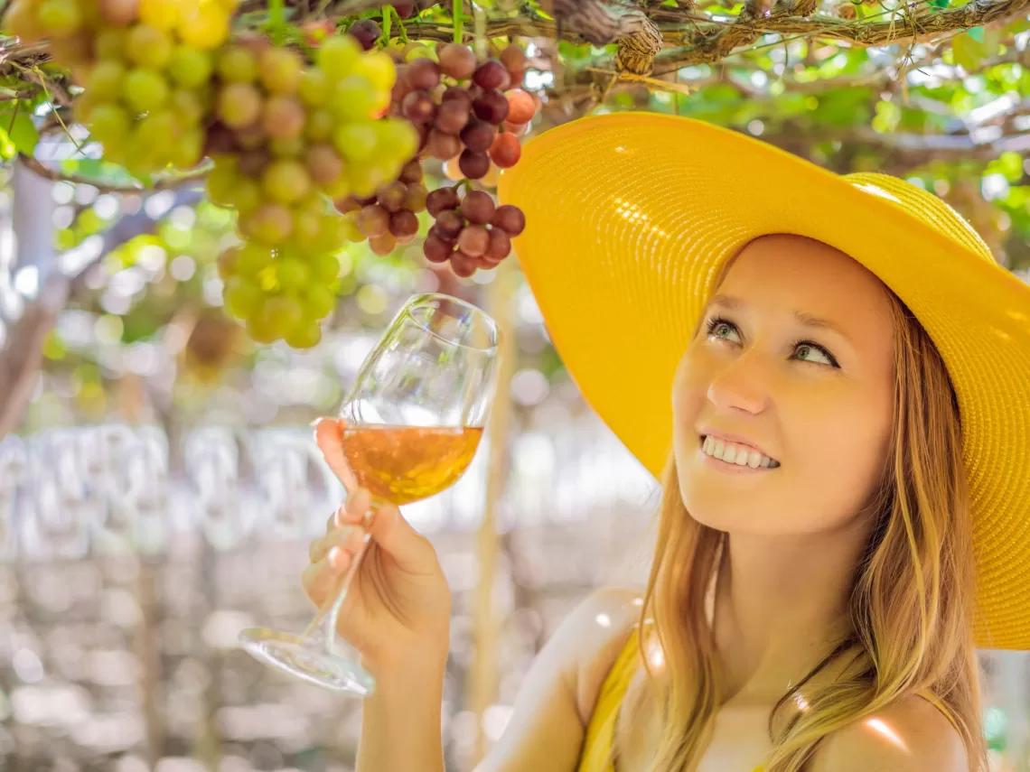 A woman standing under a grape vine while holding a wine glass.
