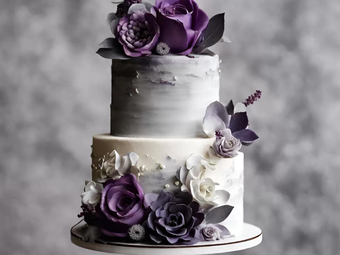 A table with a wedding cake that has purple and grey flowers on it.