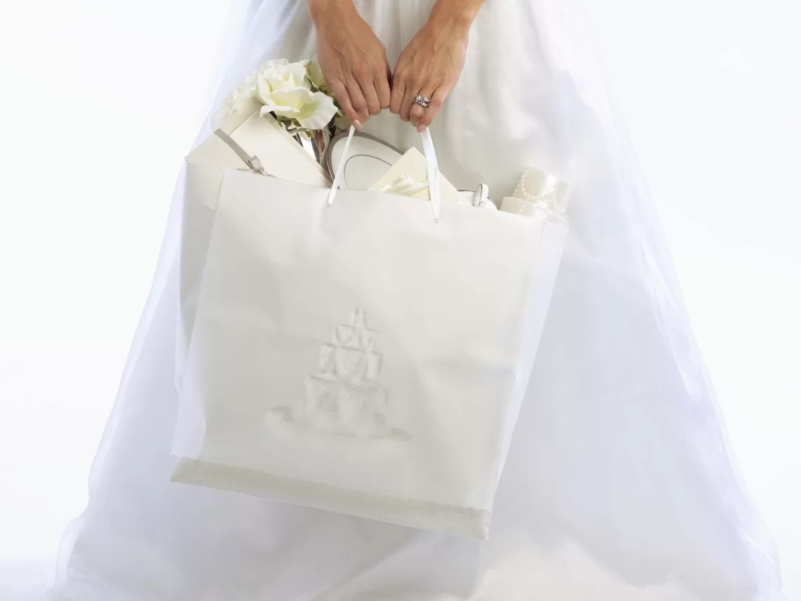A bride carrying a white gift bag filled with gifts.