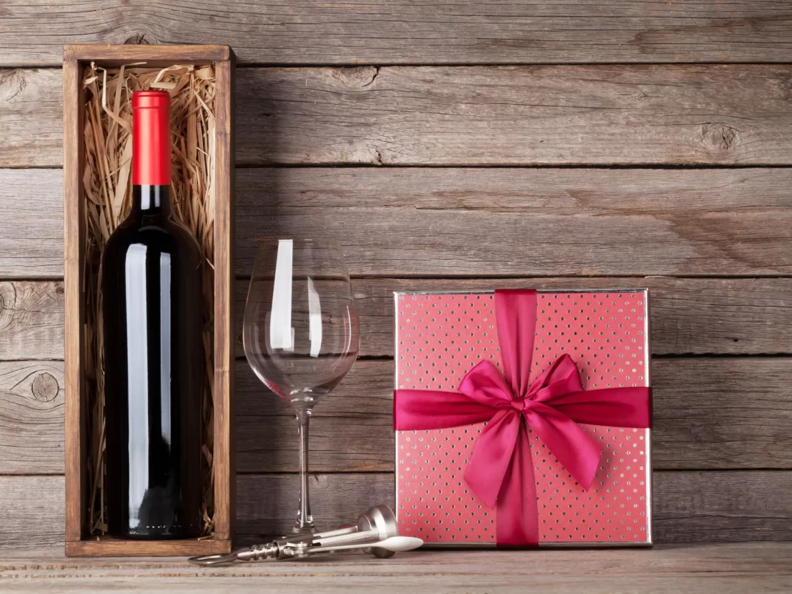 A wooden table with a wine bottle and a gift box.