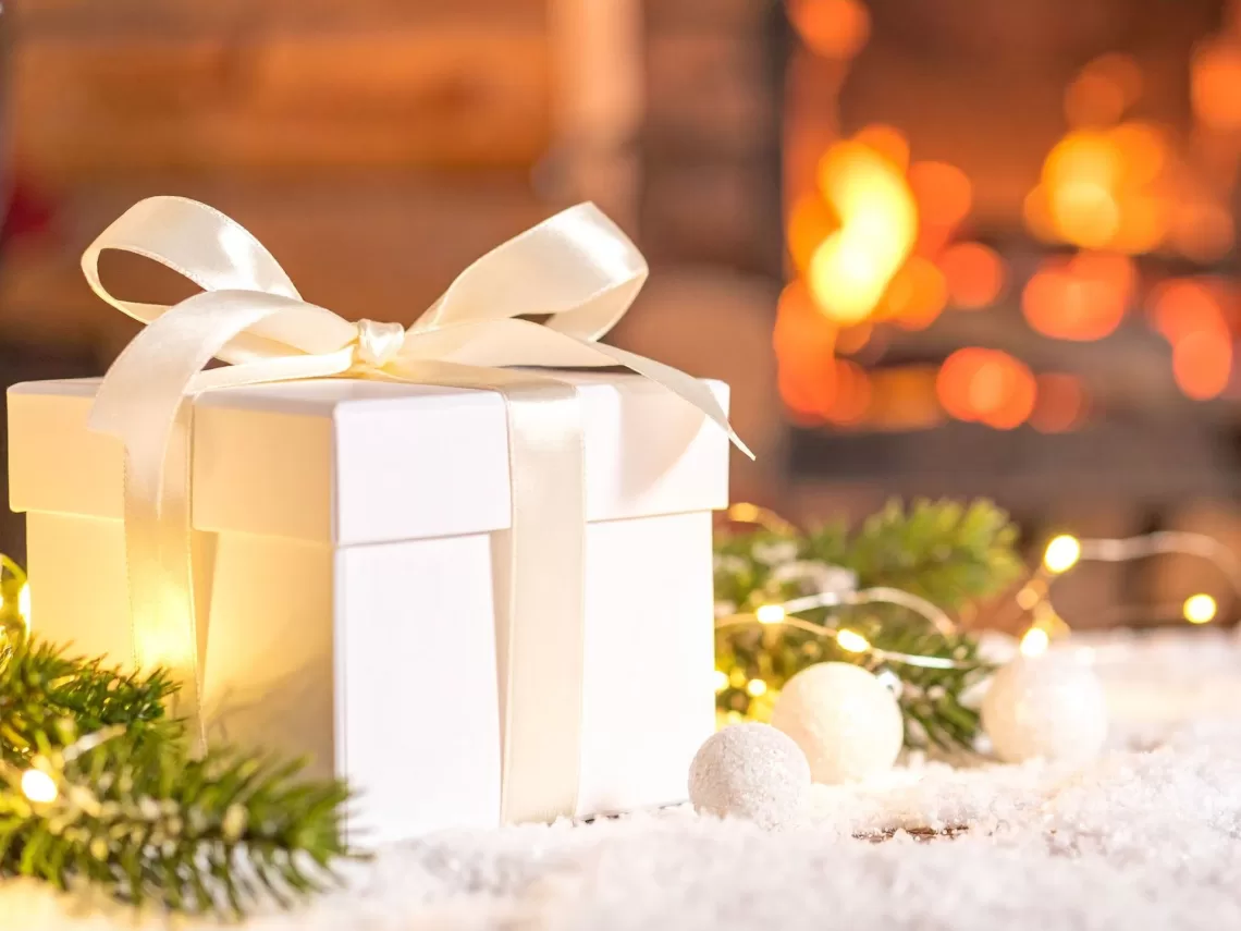 A white gift box sitting next to a lit fireplace.