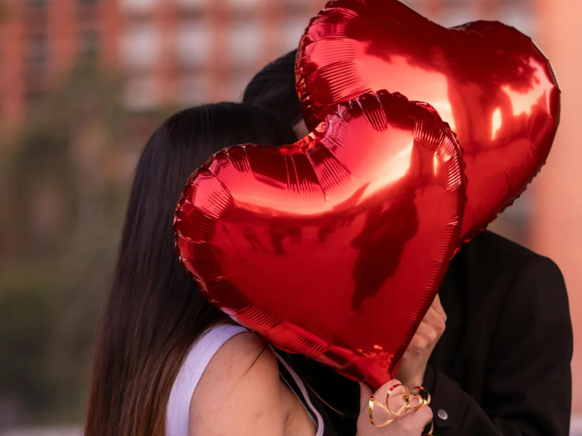 A couple holding red heart balloons.