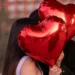 A couple holding red heart balloons.