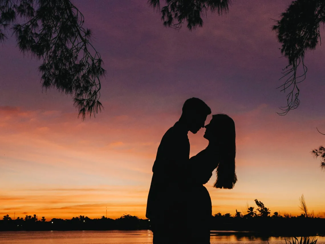 A couple standing in front of a lake with a sunset in the background.