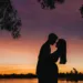A couple standing in front of a lake with a sunset in the background.