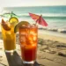 Three beach themed cocktails sitting on the sand at the beach.